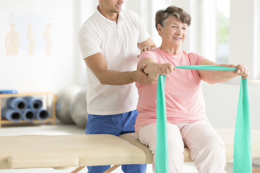 Elderly woman doing active pnf exercises with a teal scarf as a part of her rehabilitation program with a physiotherapist